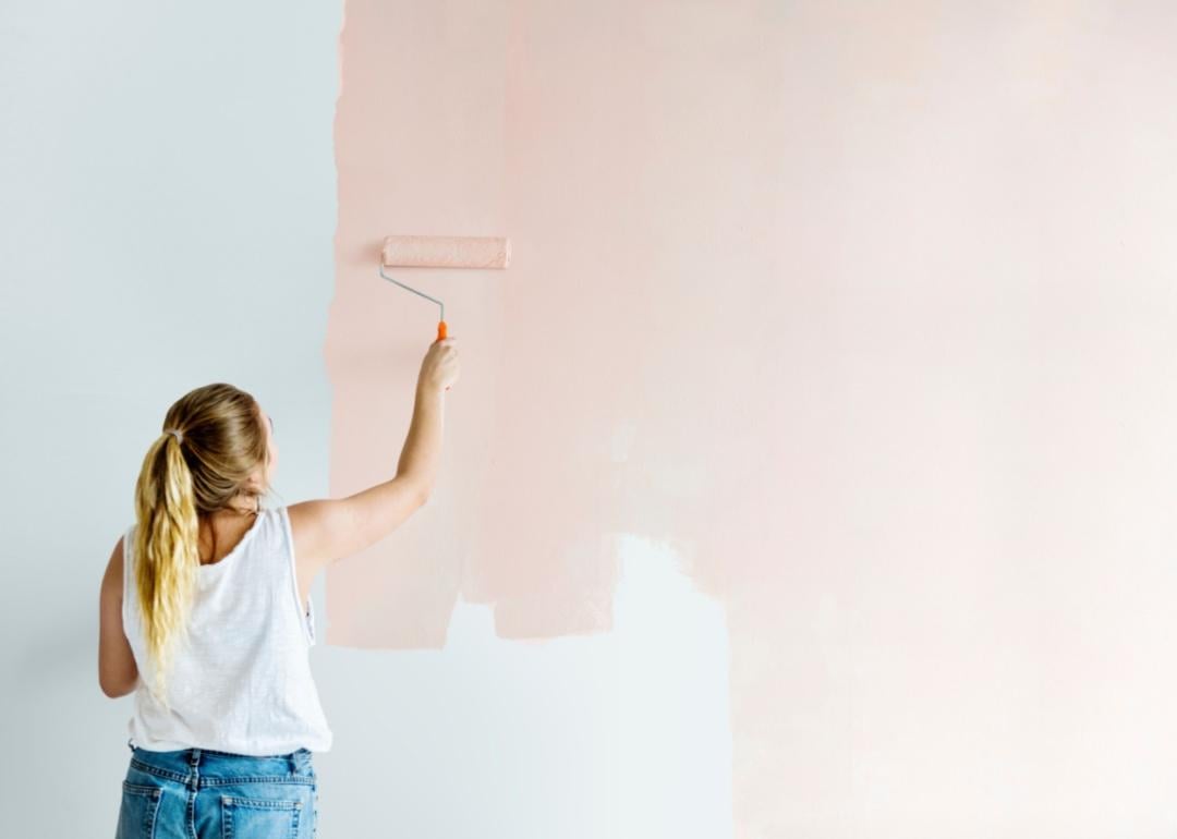 A person painting a wall pastel pink with a roller.