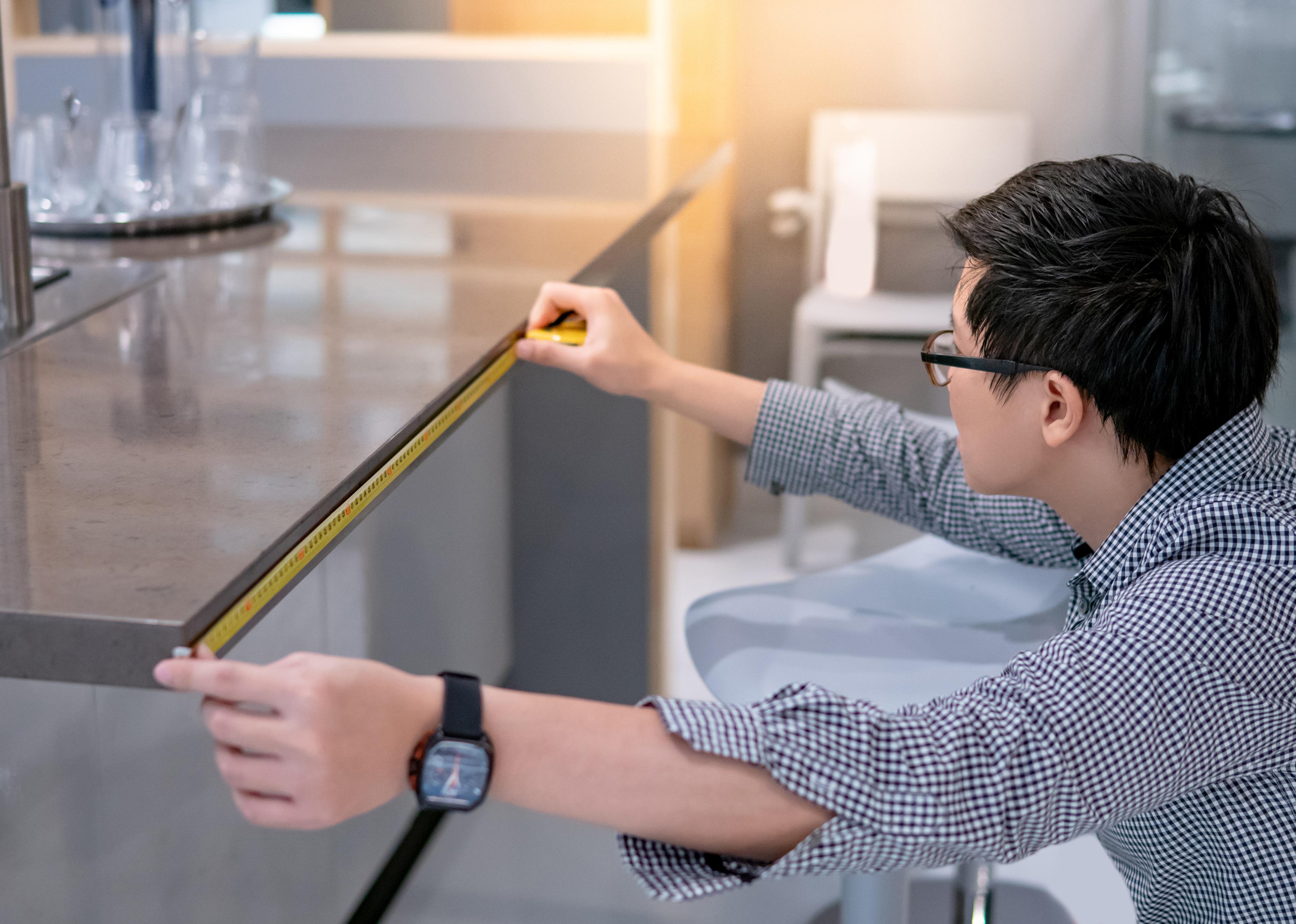 A person measures a kitchen countertop with a tape measure.