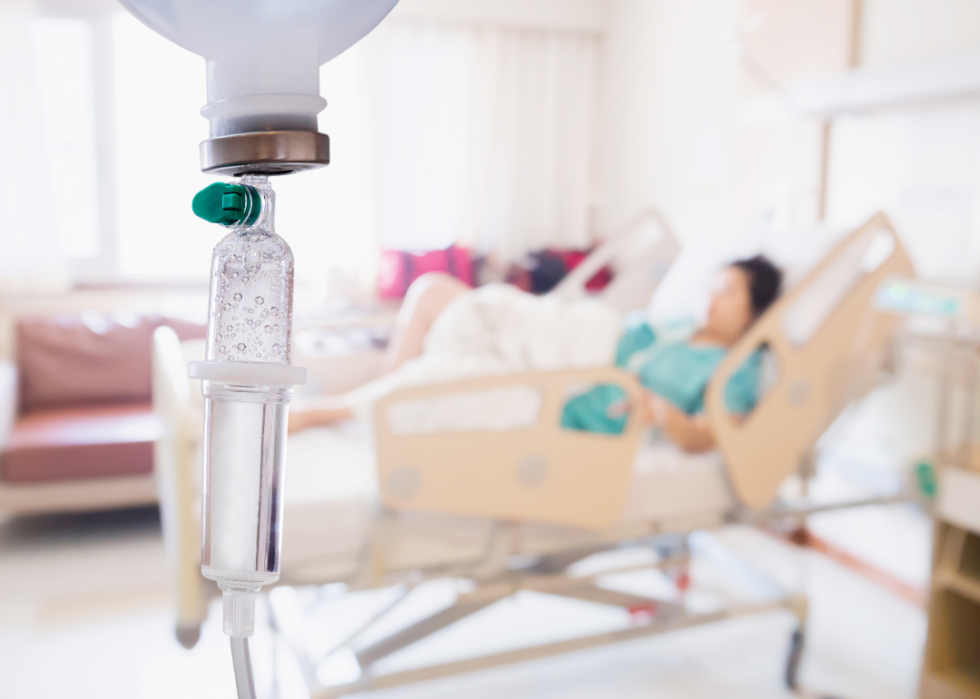 Close-up of IV drip with blurry patient in background.