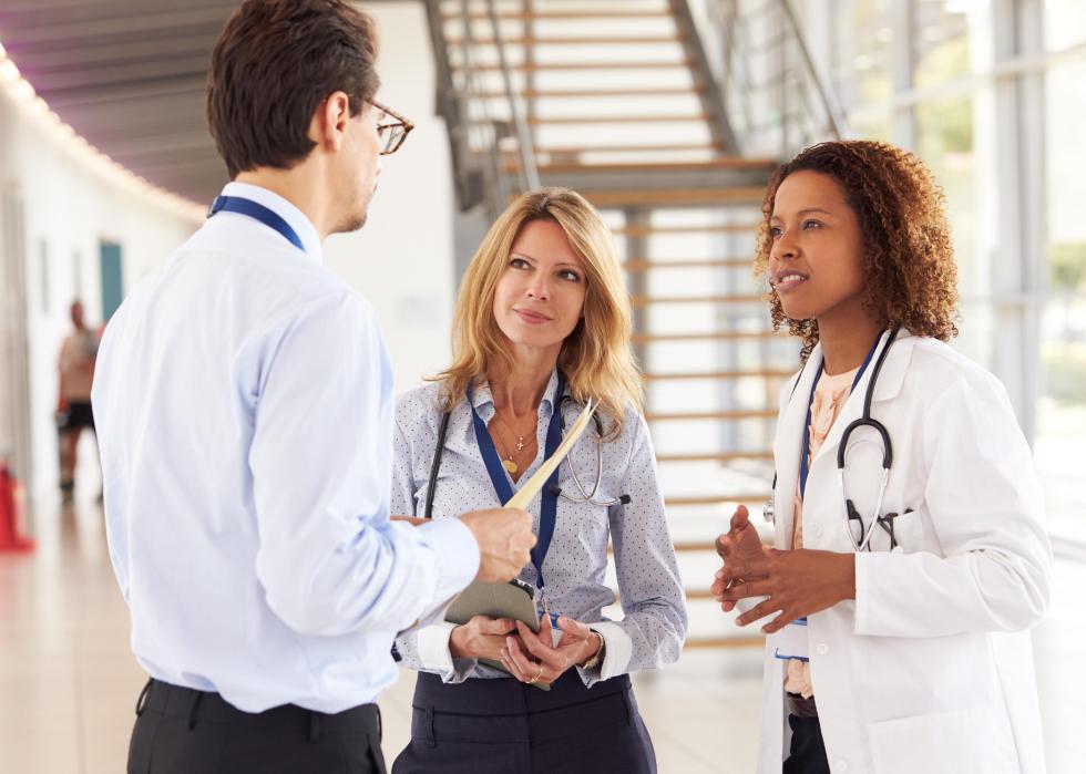 A man holding a folder talks with two women doctors.