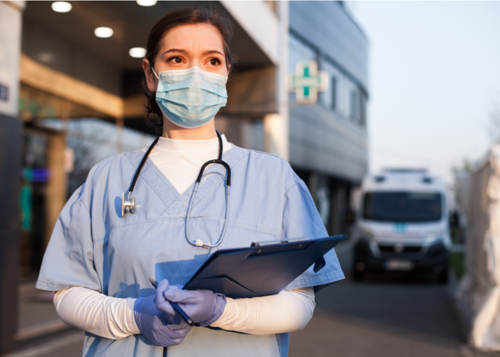 A nurse stands outside a hospital looking for someone arriving.