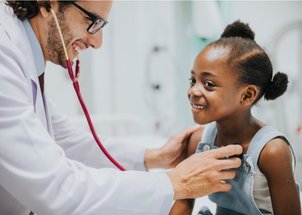 Doctor listening to a little girl's heart while they both smile.