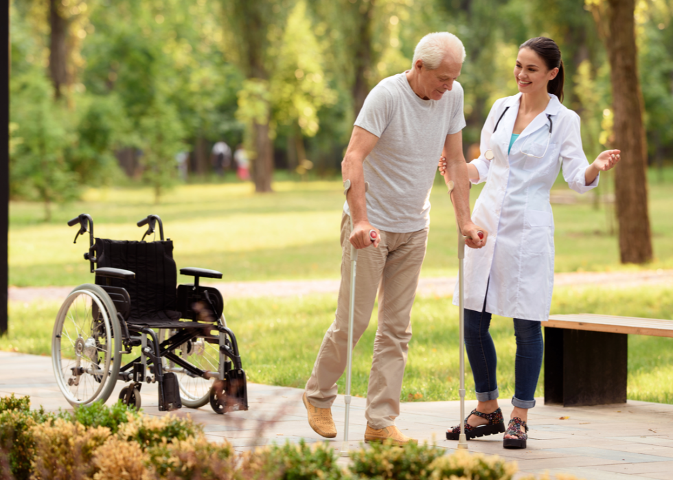 Nurse helping a patient walk from a wheelchair outside.