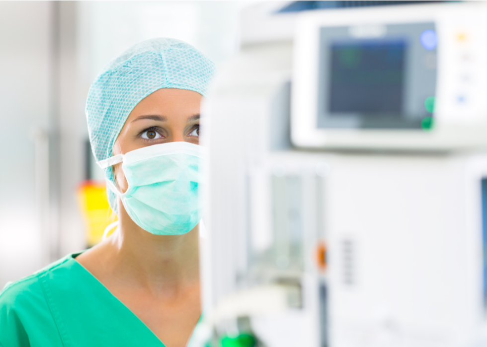 Female nurse with mask on and head covering looks at a medical screen.