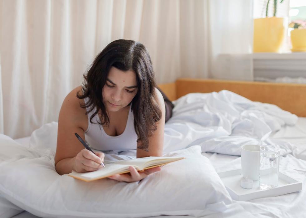 A woman writing in her journal in bed.