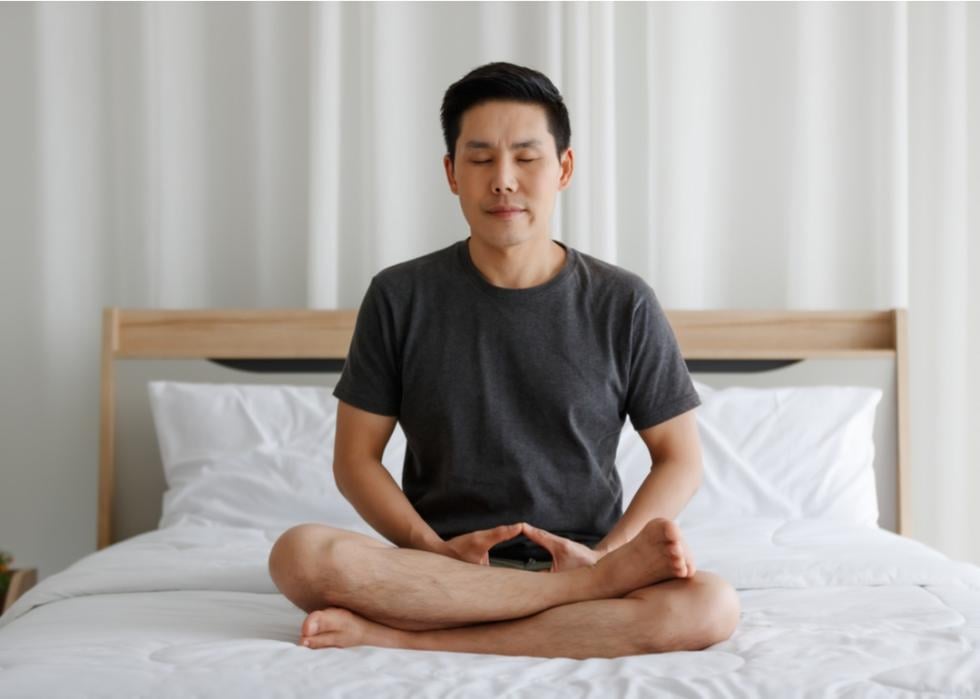 Man seated in meditation on bed.
