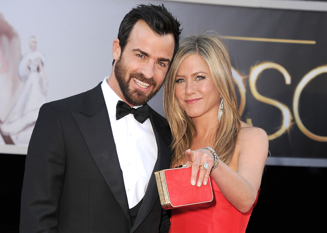 Justin Theroux in a black suit and Jennifer Aniston in a red gown on the red carpet.