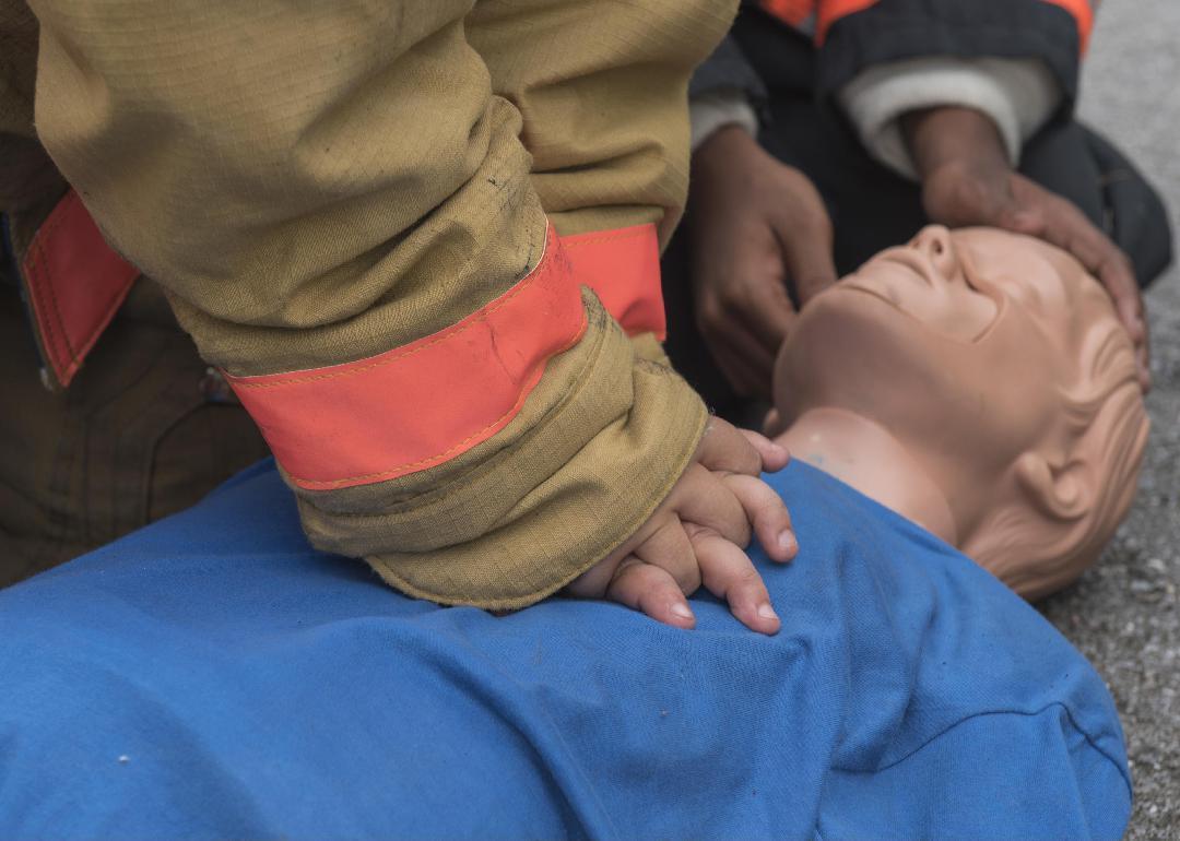 Close up firefighter's hands as they perform CPR on a dummy.