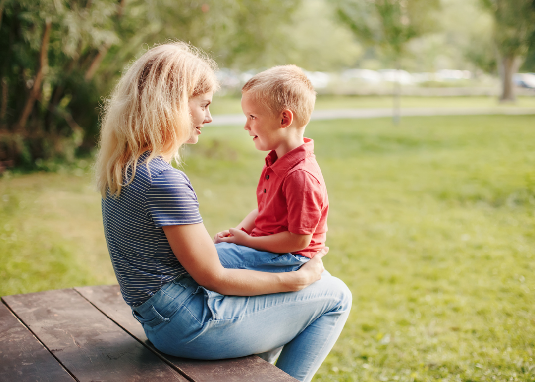 A little boy talking with his mom on her lap.