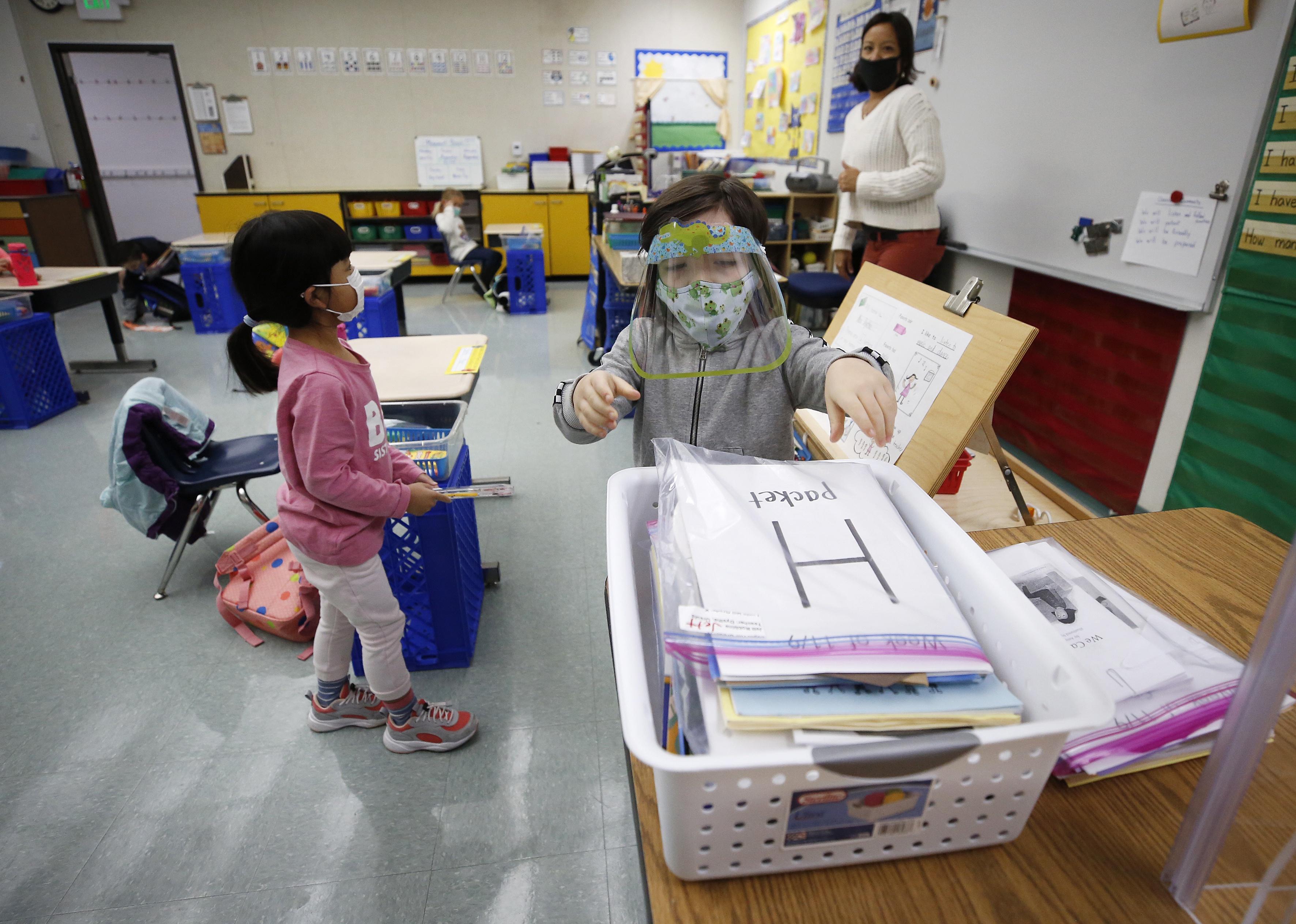 A teacher watching as her students pick up packets from a basket.