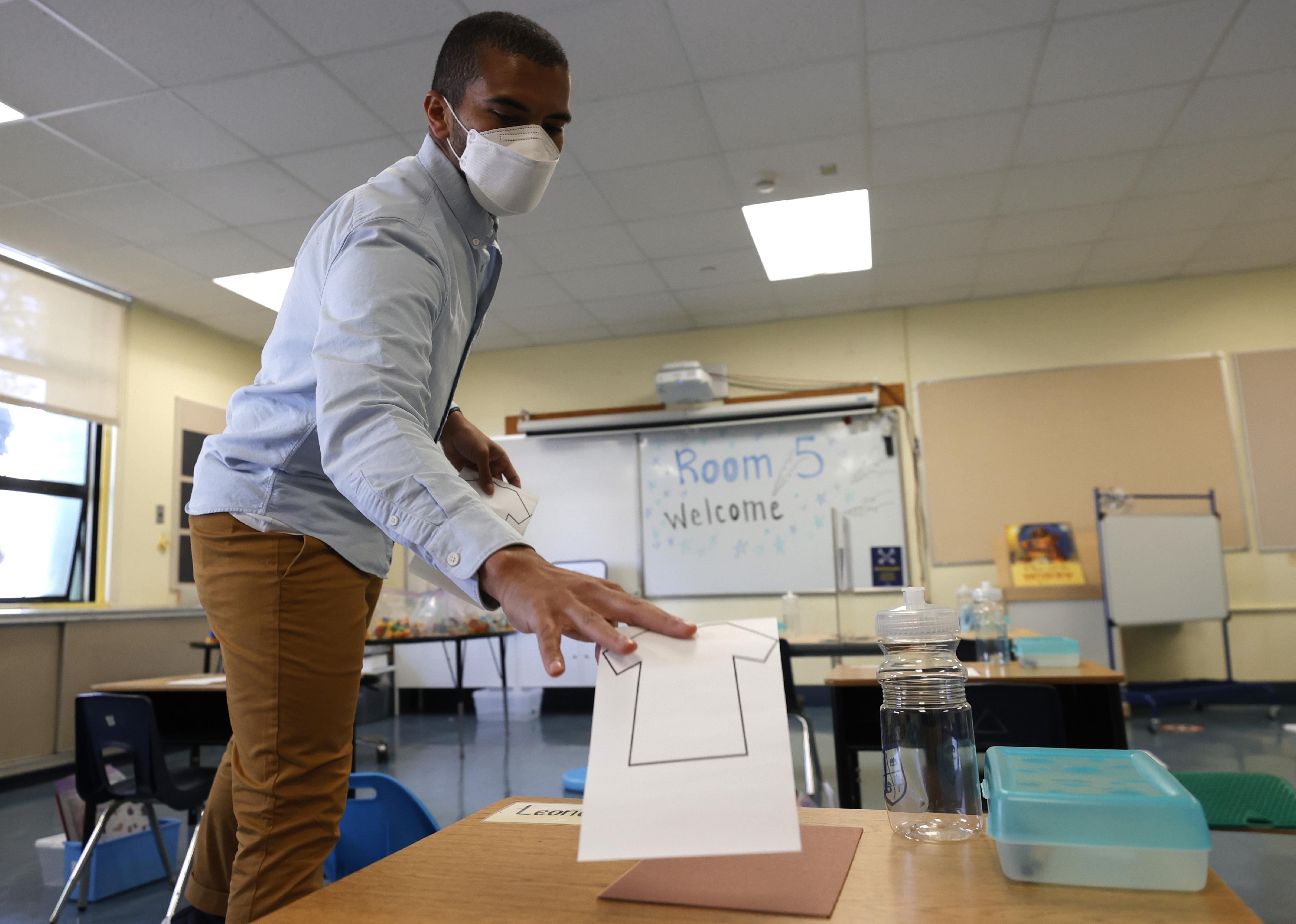 A man prepares a classroom for students by putting papers on desks.