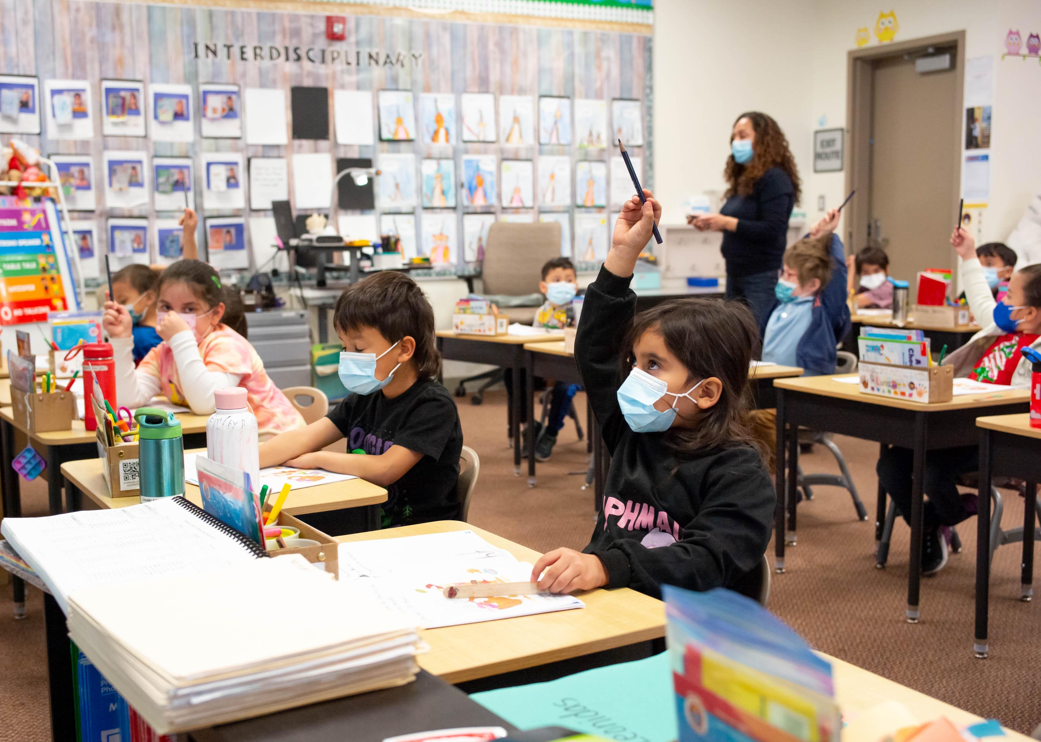 Students draw at their desks with a teacher leading in the background.