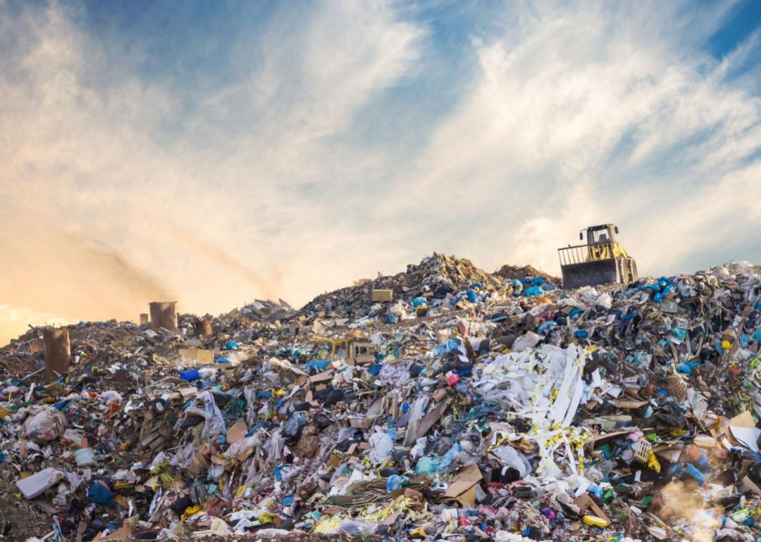 A bulldozer sits on top of a mound of garbage in the landfill.