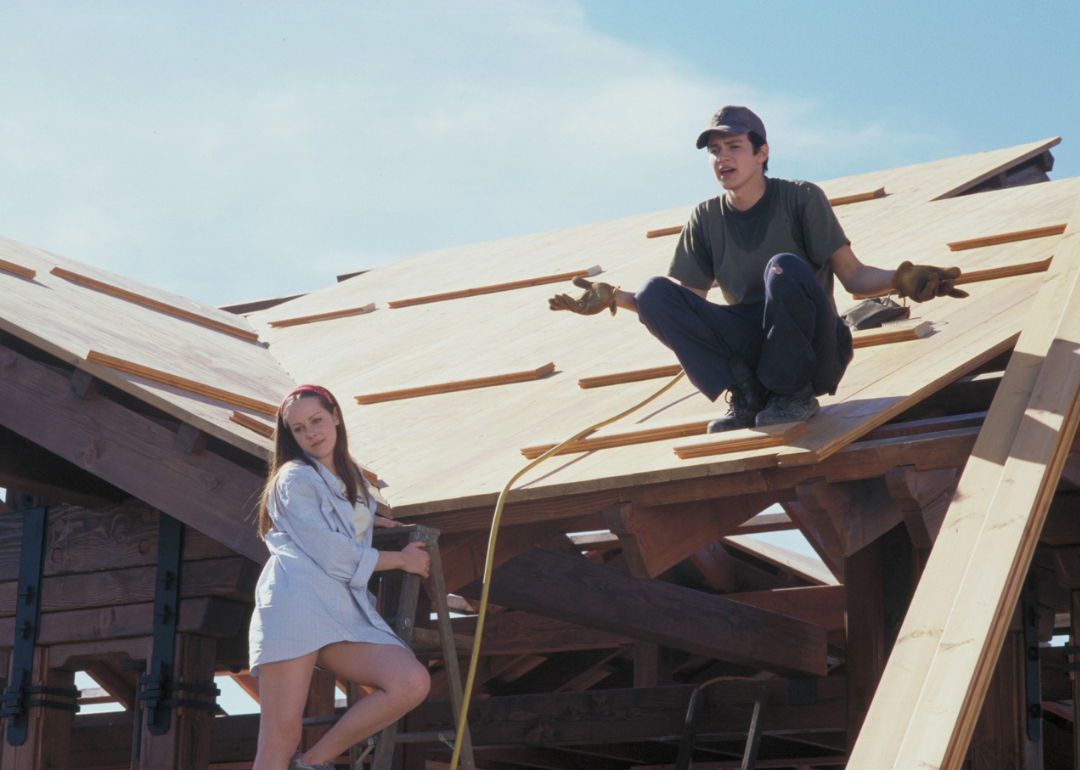 Jena Malone on a ladder next to Hayden Christensen working on a roof.
