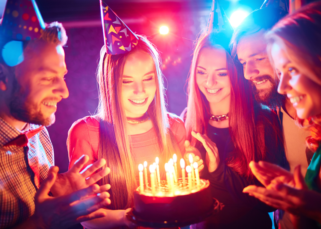 Friends gathered around a birthday cake with lit candles. 