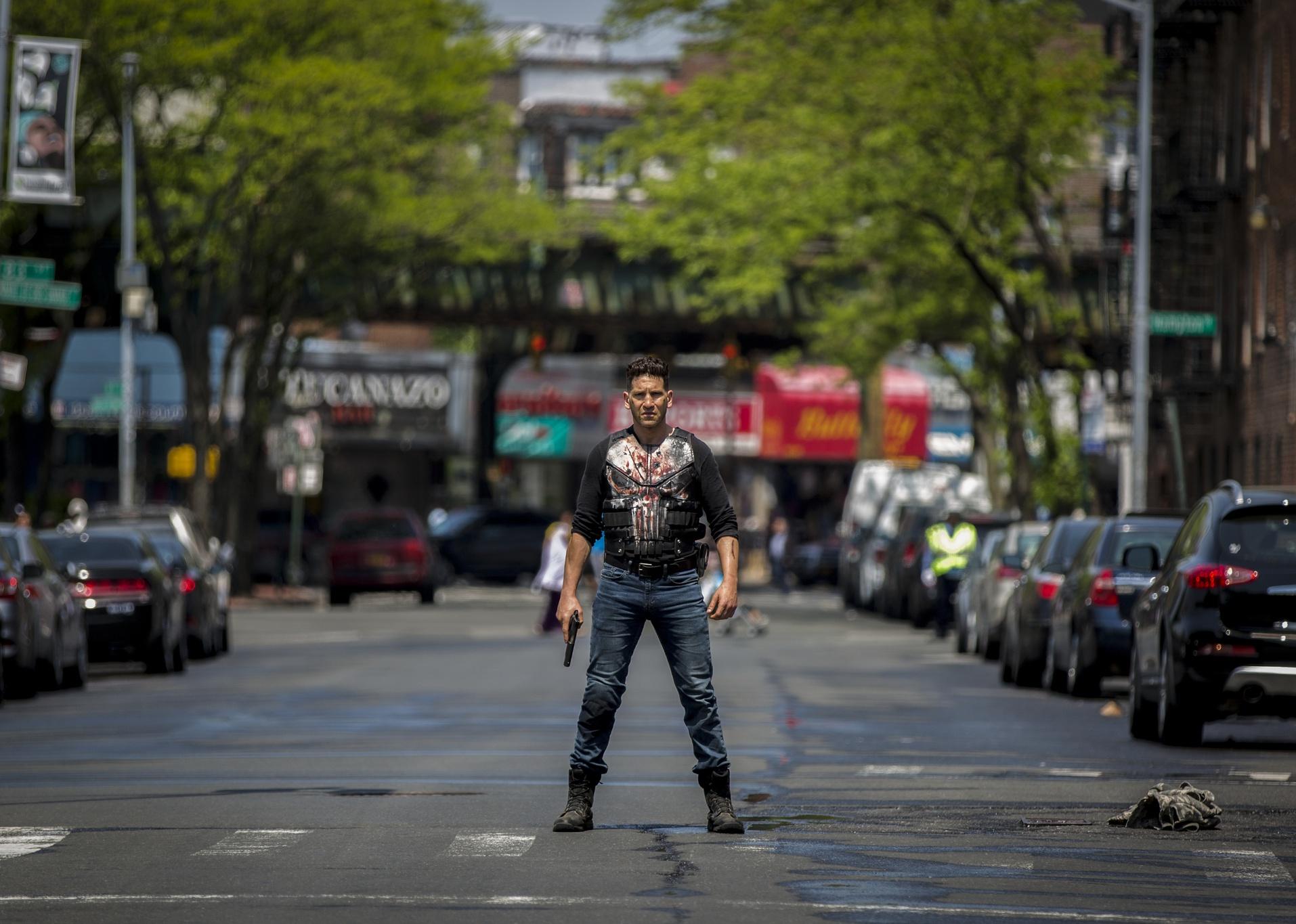 Jon Bernthal standing in the middle of the street with a gun.