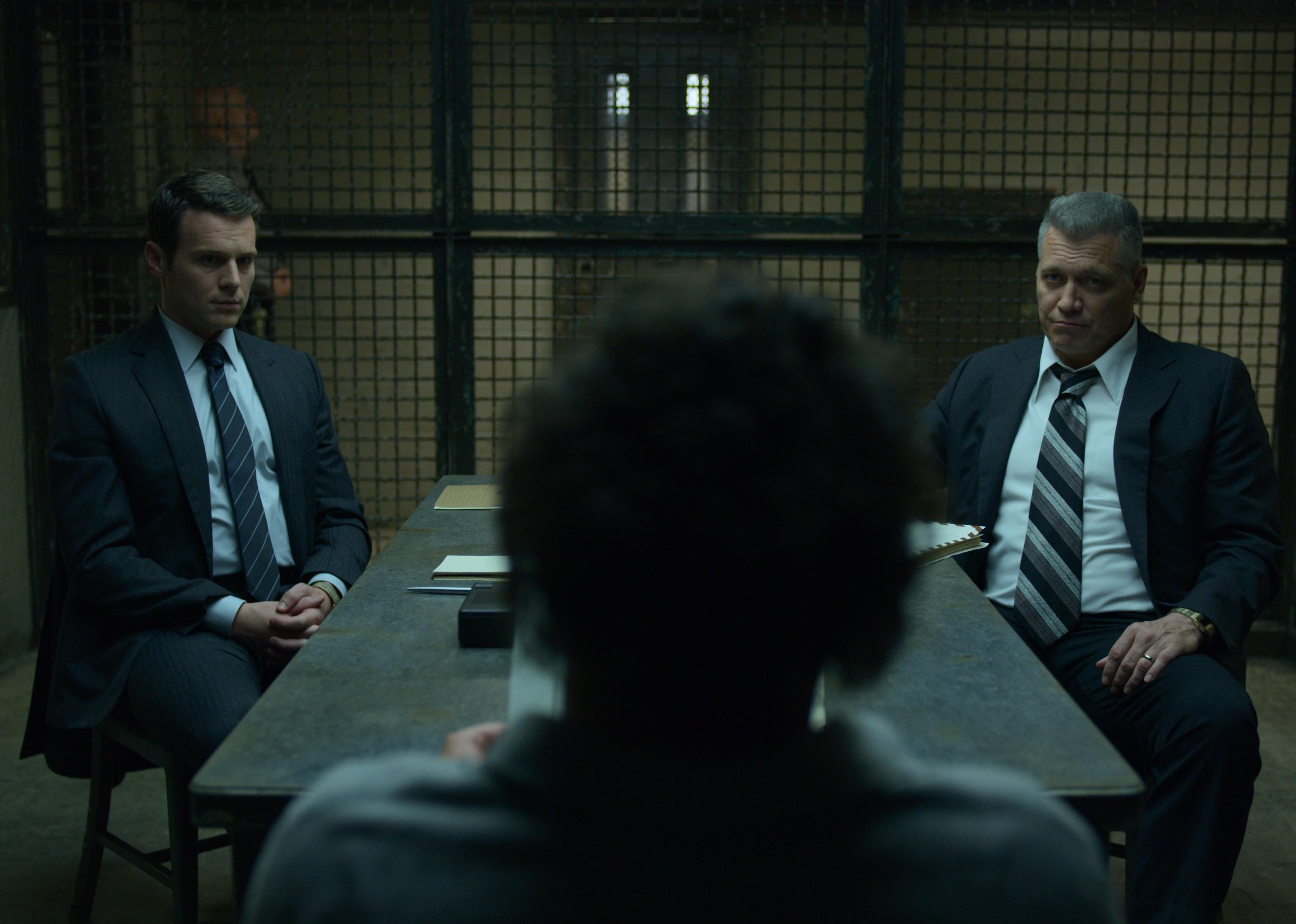Two men in suits interview a prisoner.