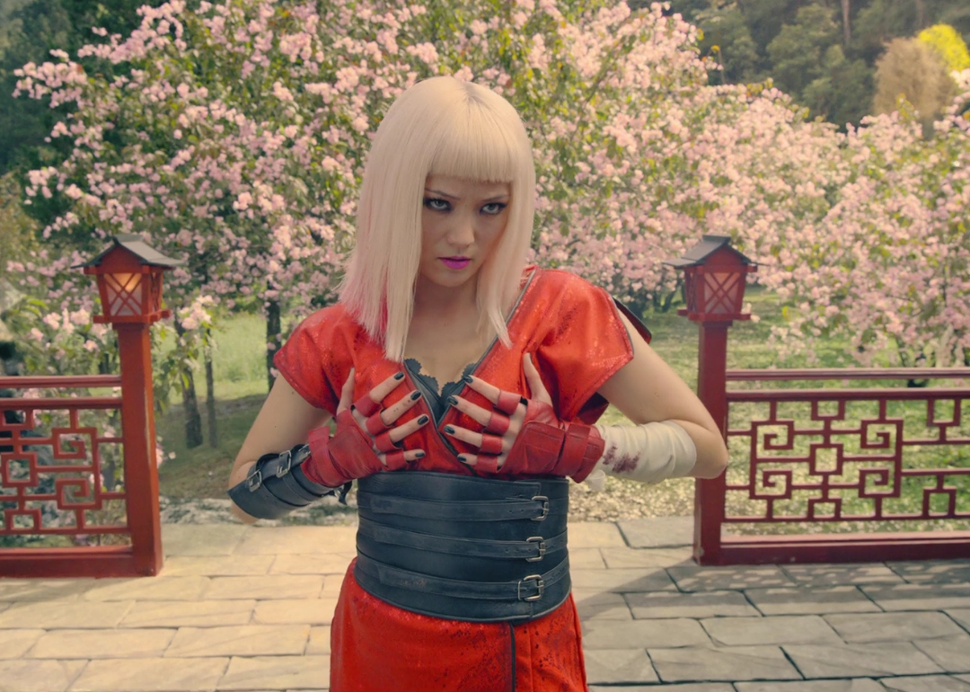 A blonde girl in red fighting gear in front of a blossoming cherry tree.