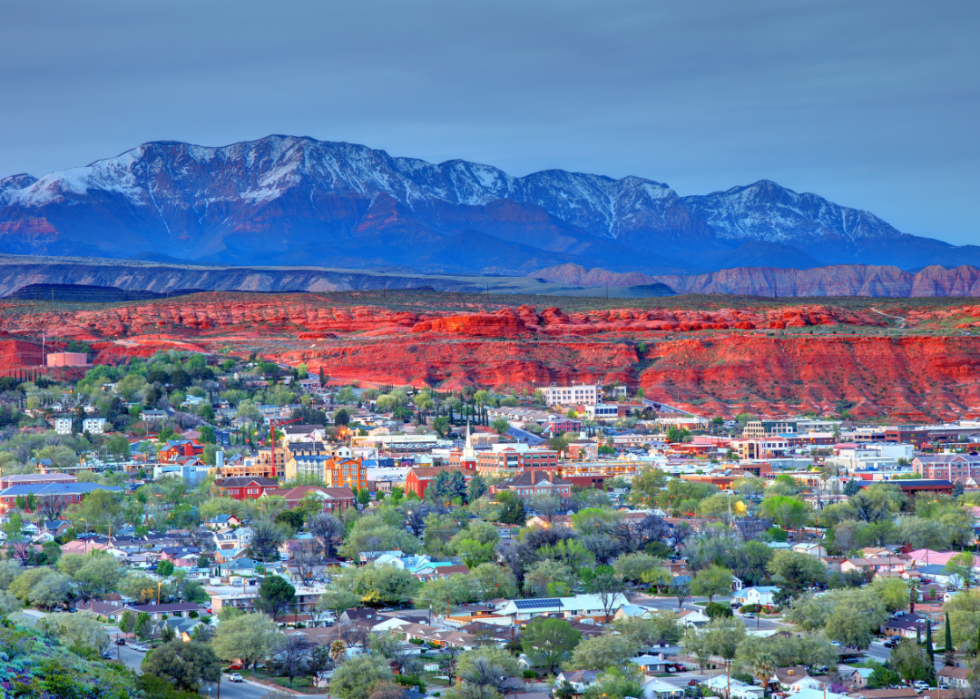 Aerial view of homes and buildings in St. George, Utah with orange mesa and snow-capped mountains in the background.