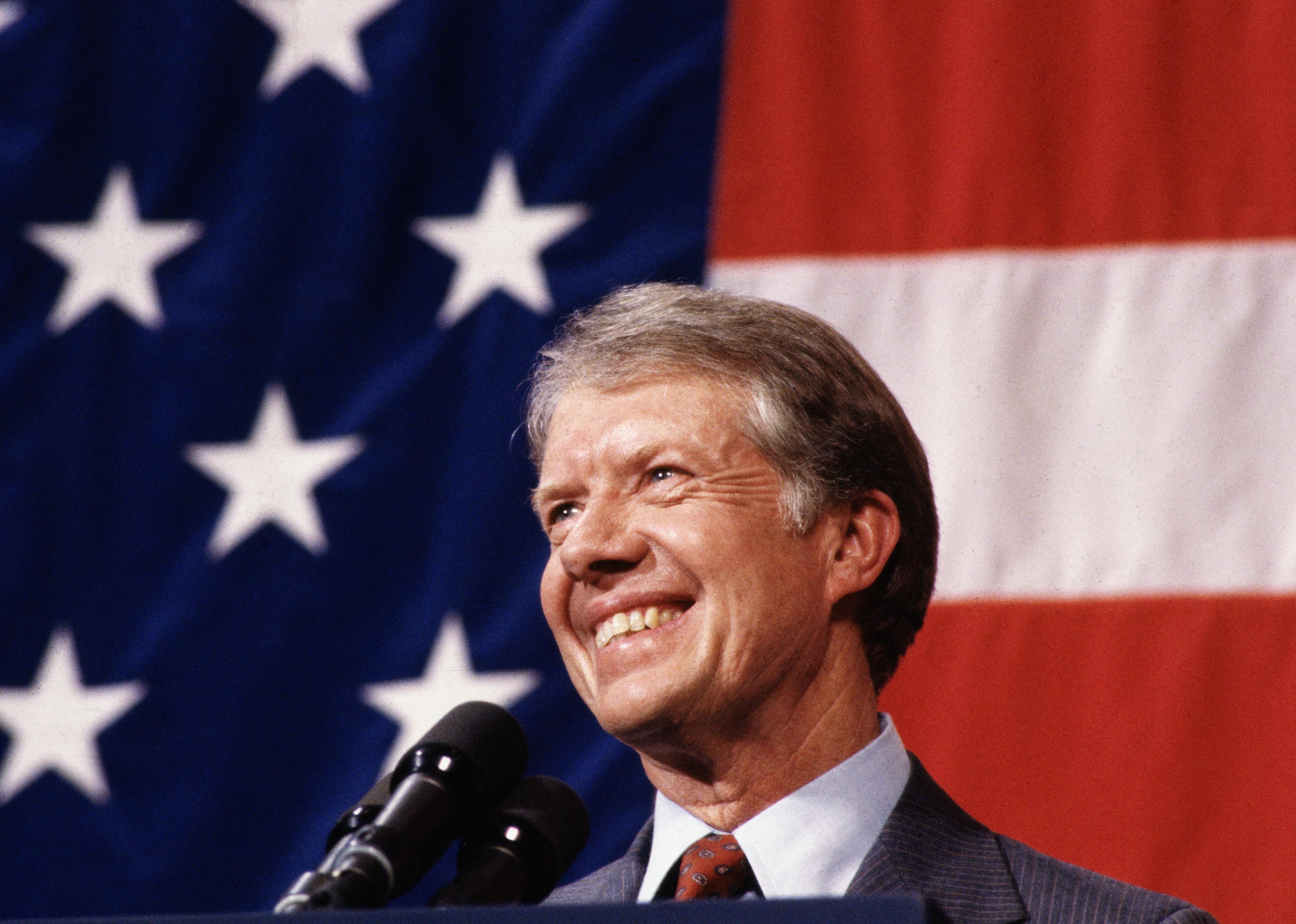 Jimmy Carter smiling at a podium in front of an American flag.