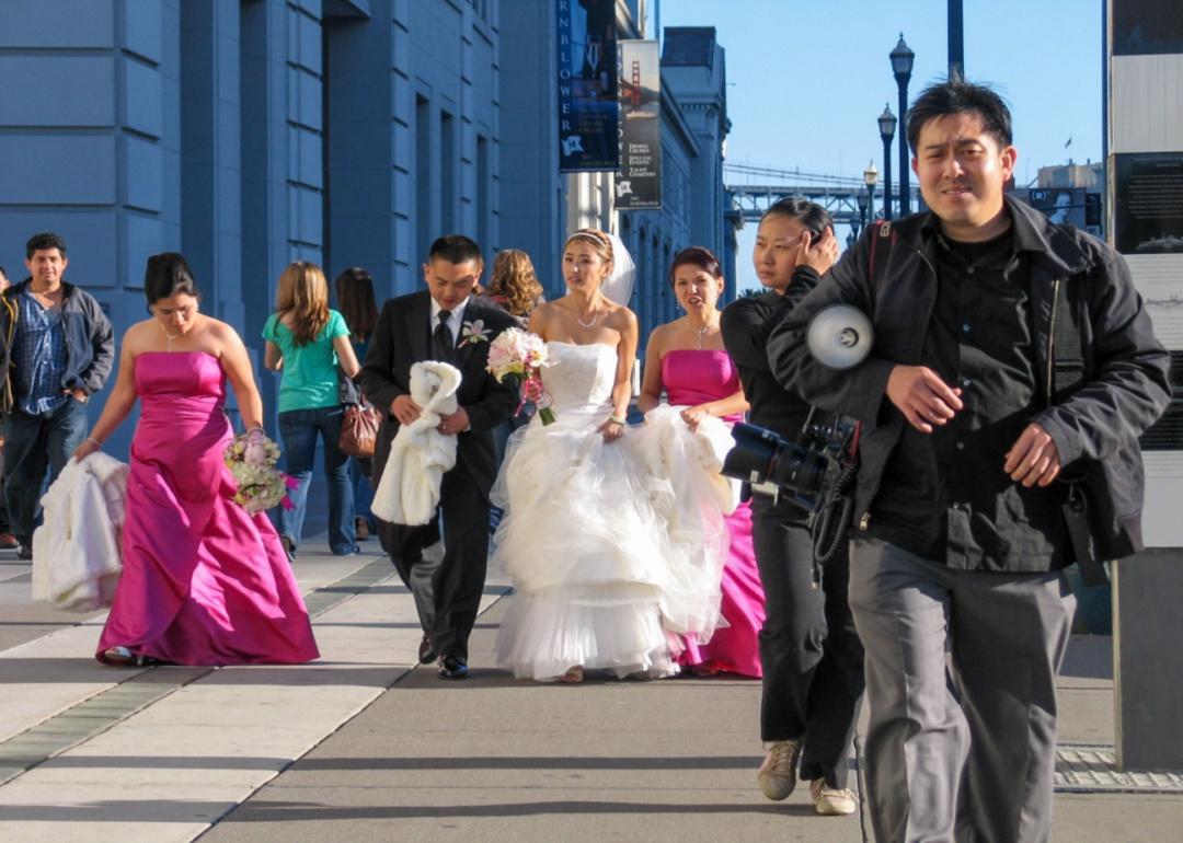 A photographer walks in front of a wedding party on a San Francisco street.