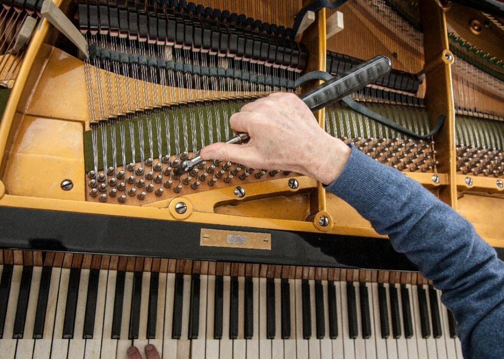 A man uses a tool to tune a piano.