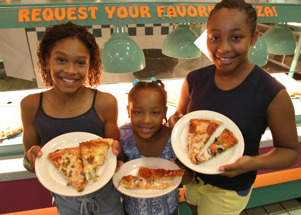 Three girls holding plates of pizza.
