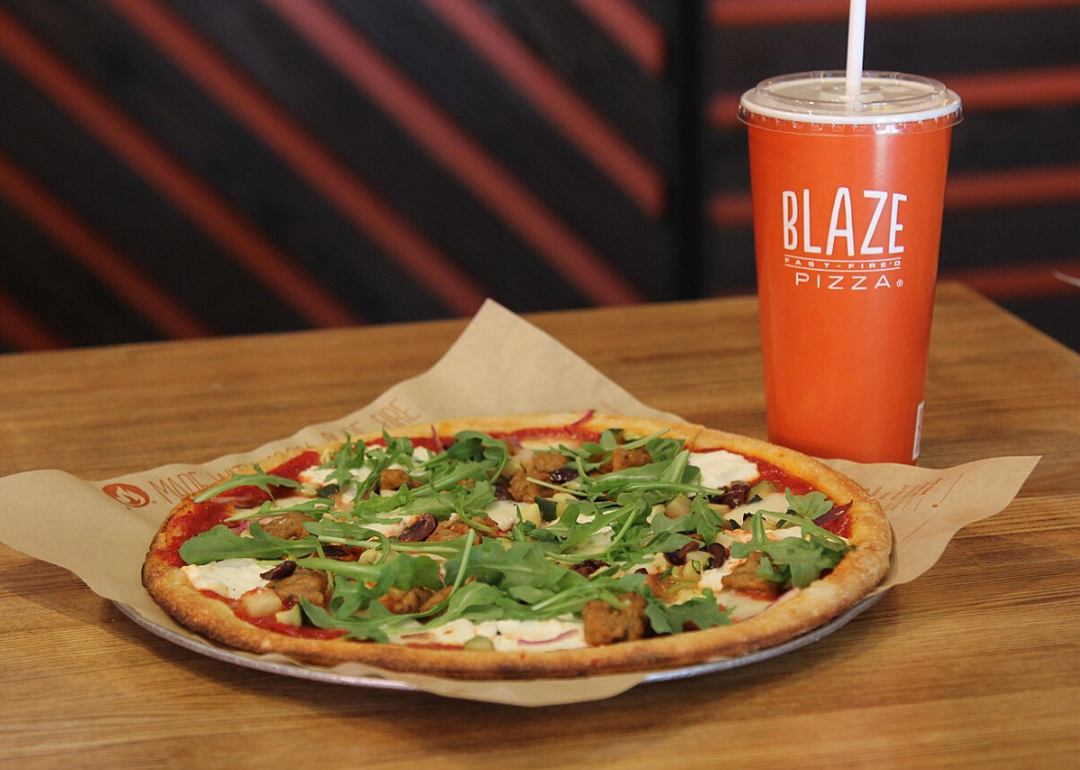 A pizza topped with greens and a Blaze soda cup.