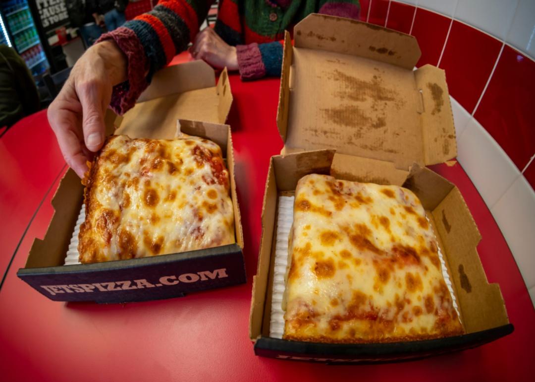 A person grabs a small square Jet's pizza from a box.