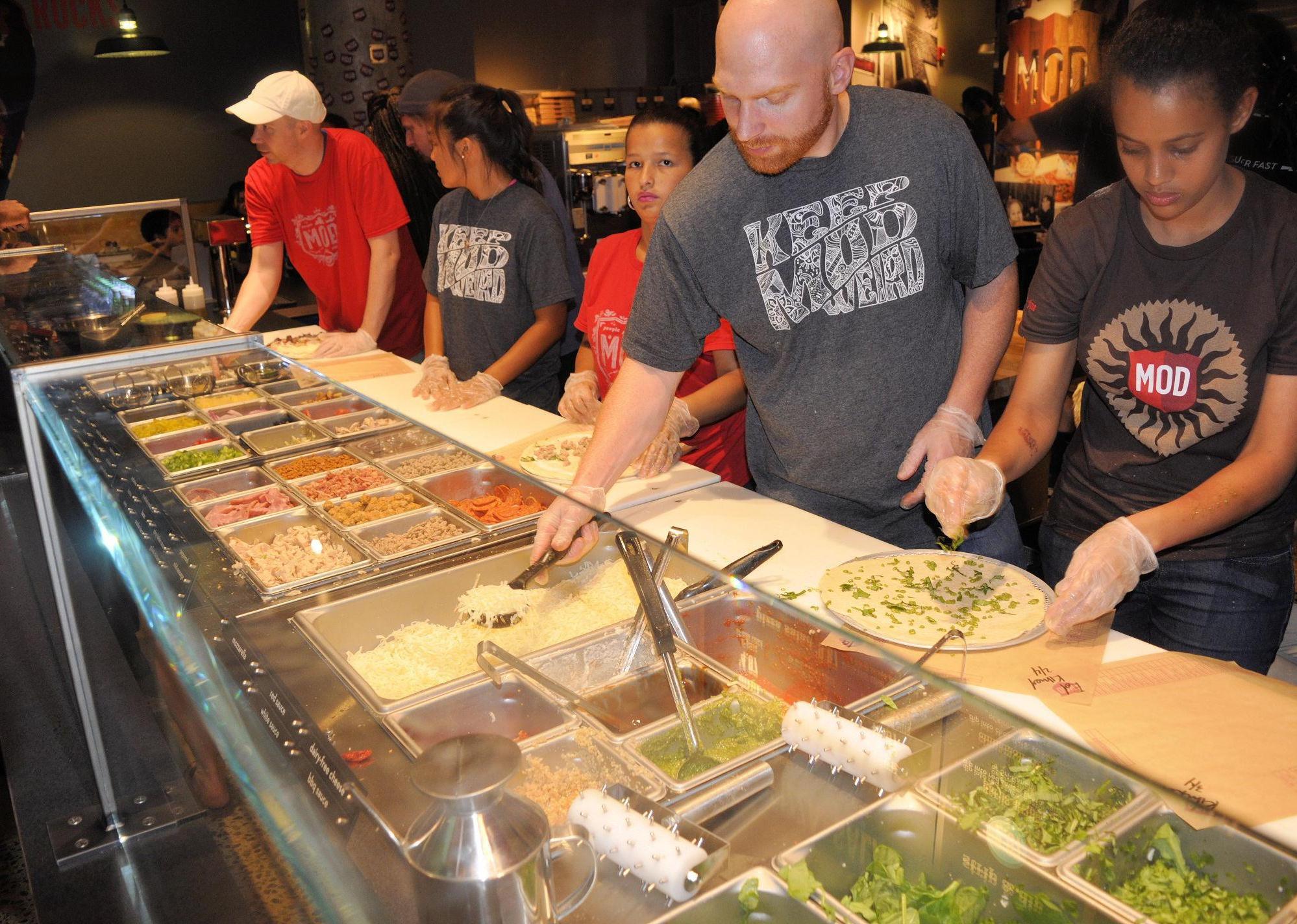 Employees adding ingredients to pizza in a line at Mod.