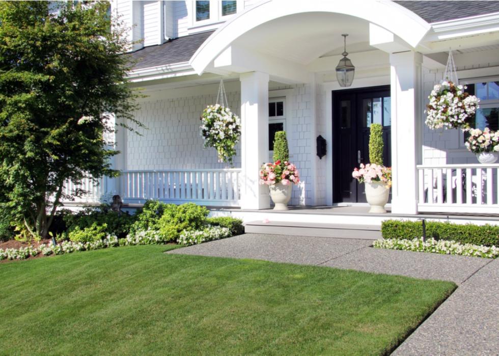 Big white home with hanging planters and lush landscaping.