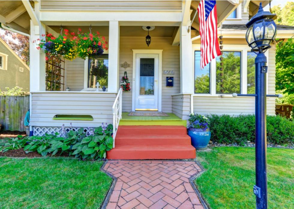 Tan colonial home with flowers and flag.