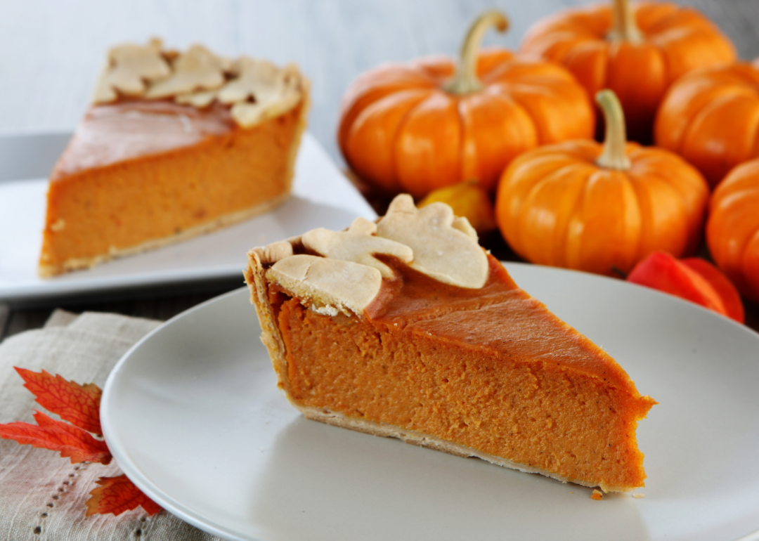 Two slices of pumpkin pie with tiny pumpkins in the background.