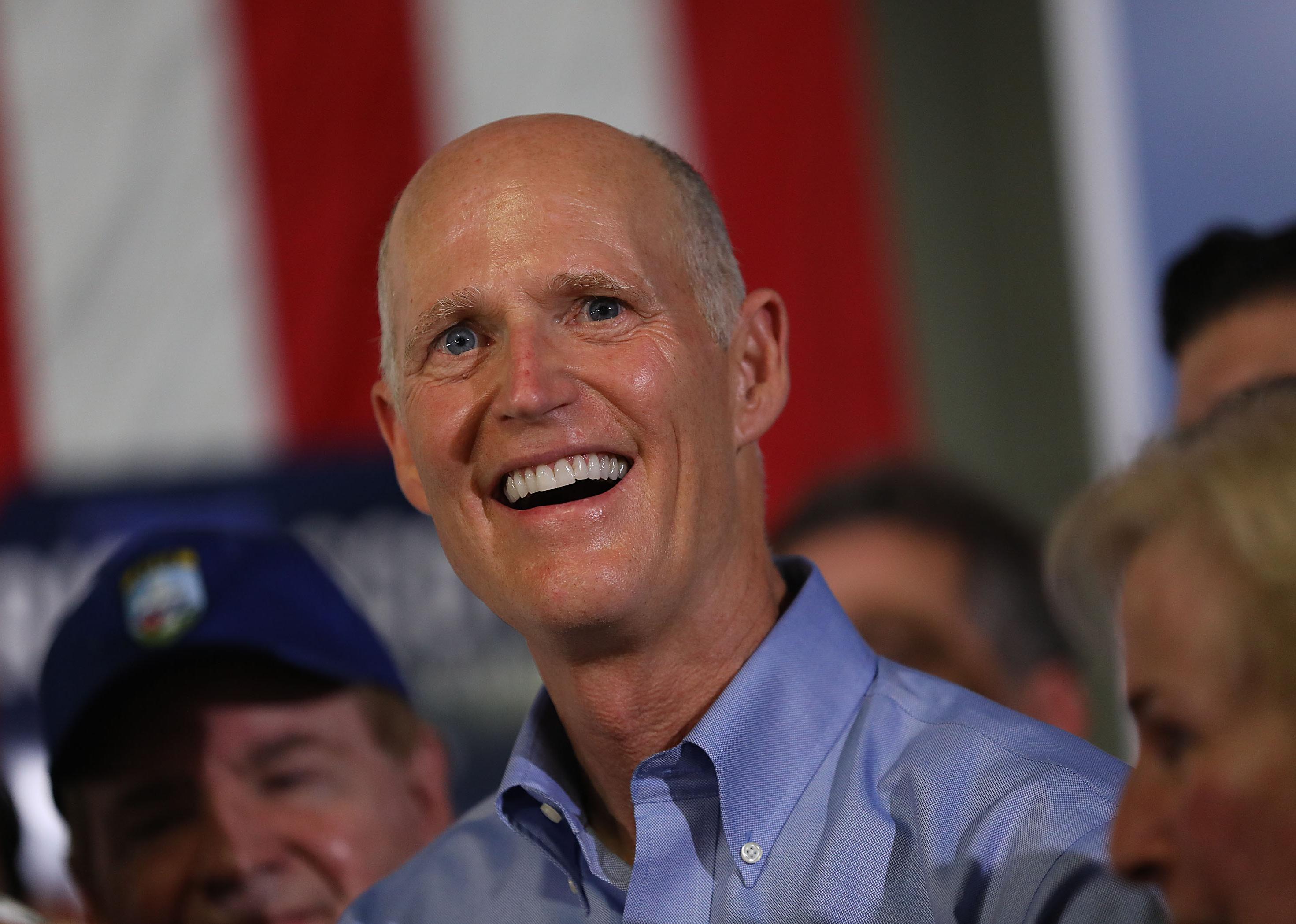 Rick Scott smiling in front of an American flag.