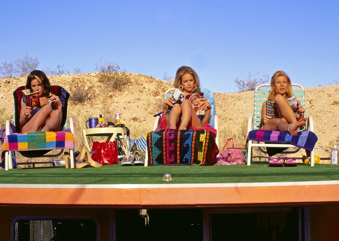 Gwyneth Paltrow, Kelly Preston, and Christina Applegate in swimsuits and sitting in beach chairs reading magazines.