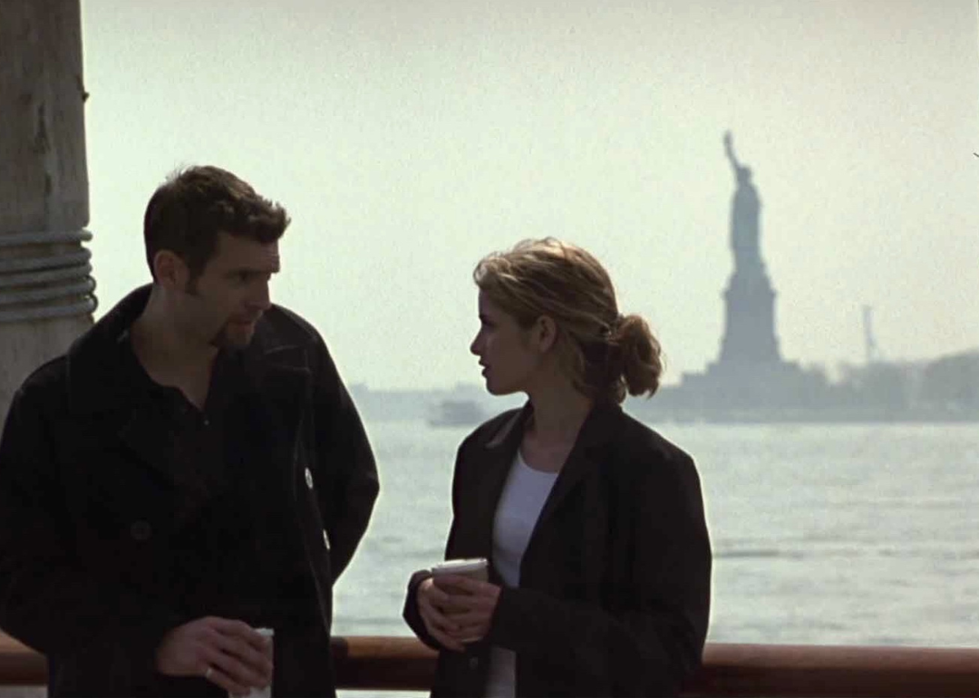 Amanda Peet talking to a man with the statue of liberty in the background.
