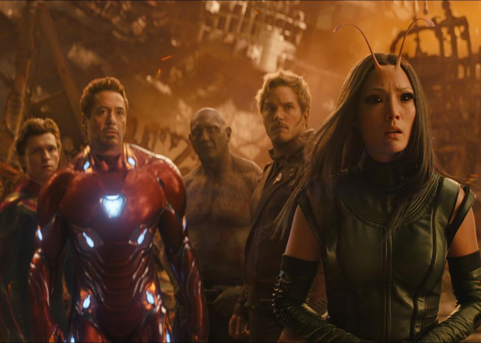 A group of Avengers (woman with black eyes and antennae, man in red armor, boy in spider man suit, others in background.) looks ahead in wonderment.
