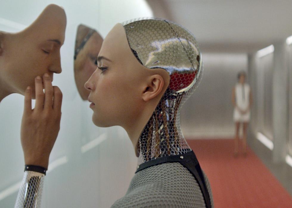 A robot with human skin and face looking at another replica like herself.