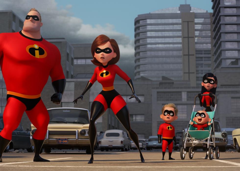 The Incredibles family in red superhero suits stand looking up at something.