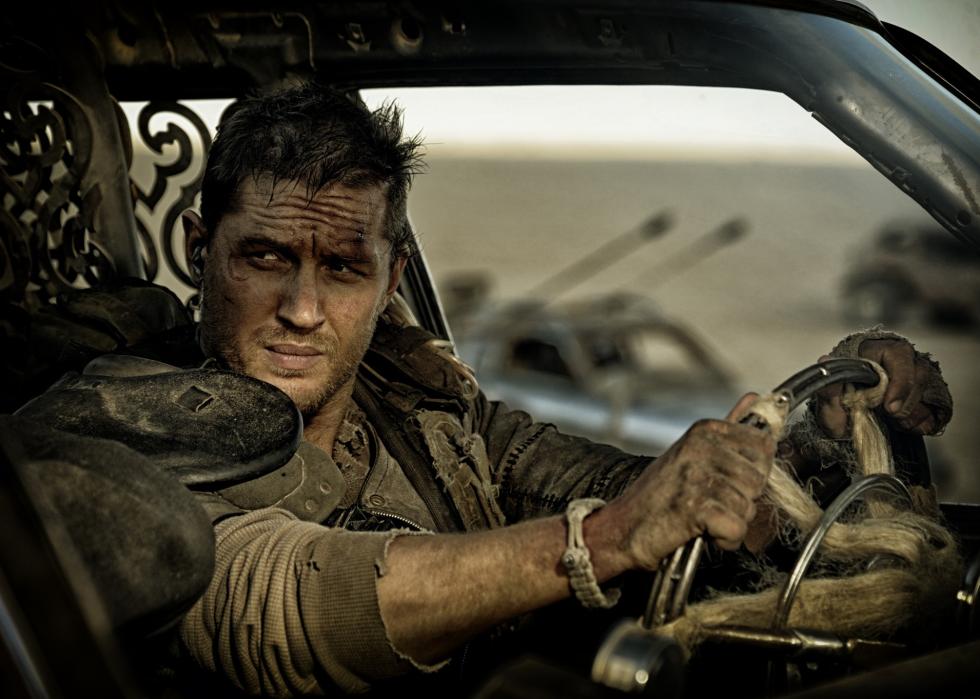A man in an old car in tattered clothing.