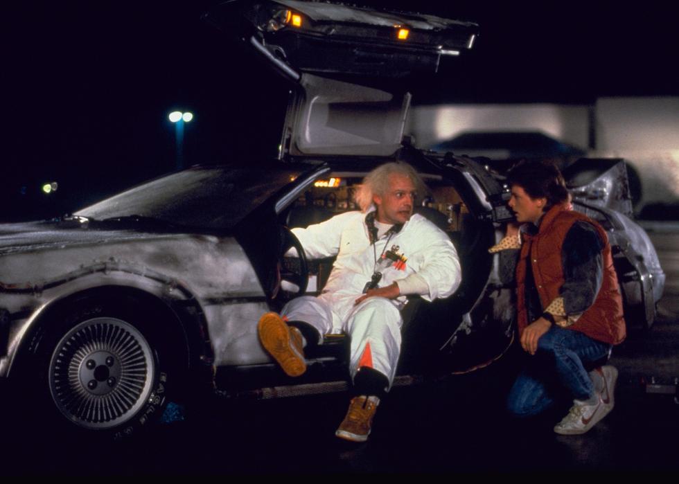 A young man talks to an old man with crazy hair wearing a white suit and driving a Delorean.