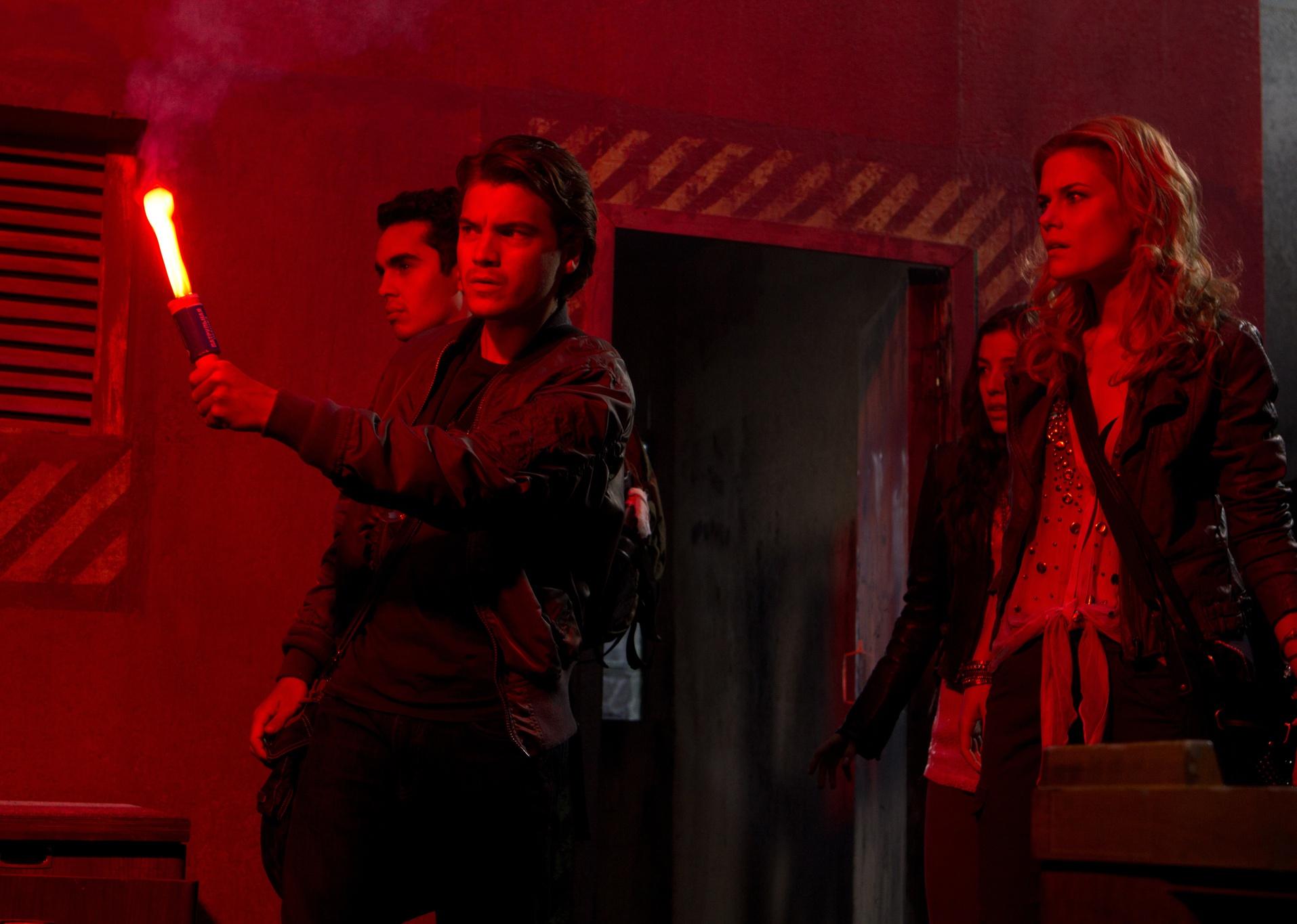 Four young adults walk through a red lit hallway.