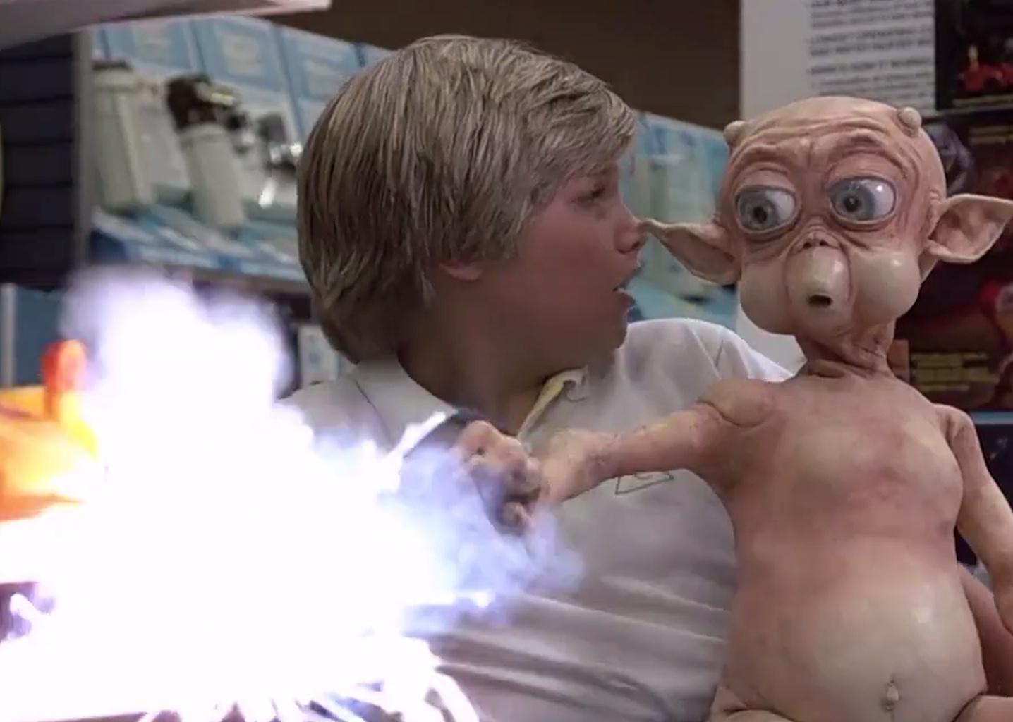 A blonde boy with an alien in his lap shooting light at something.