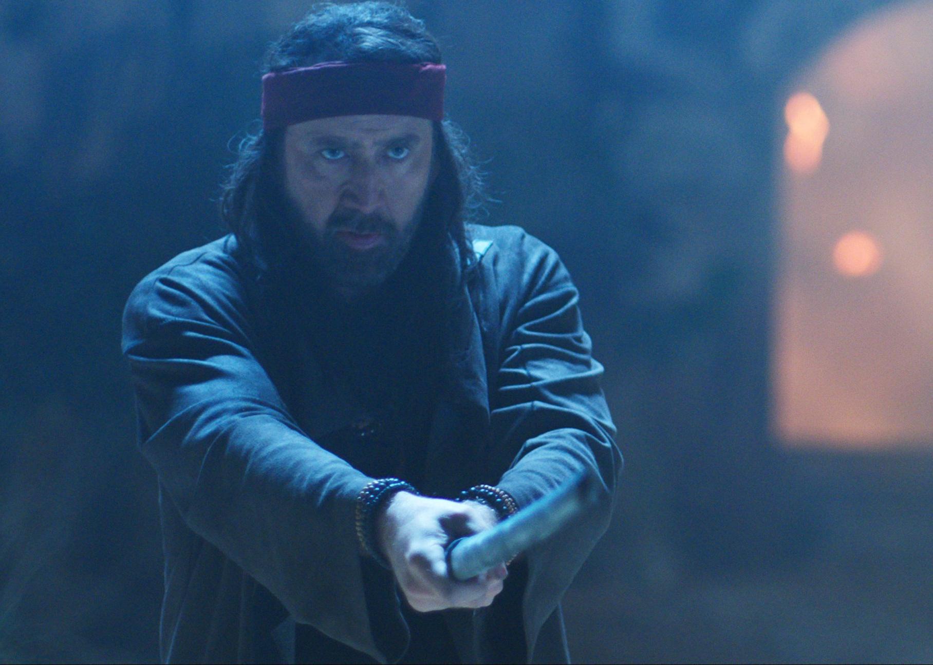 Nicolas Cage with a red bandana wrapped around his head holding a sword in front of him.