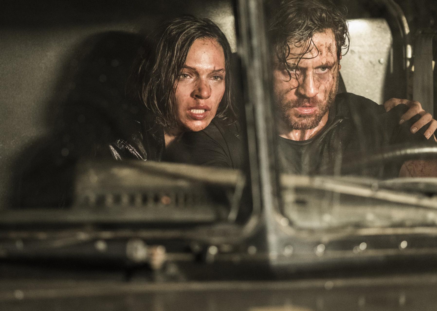 A man and woman looking tired, dirty and scared driving a truck.
