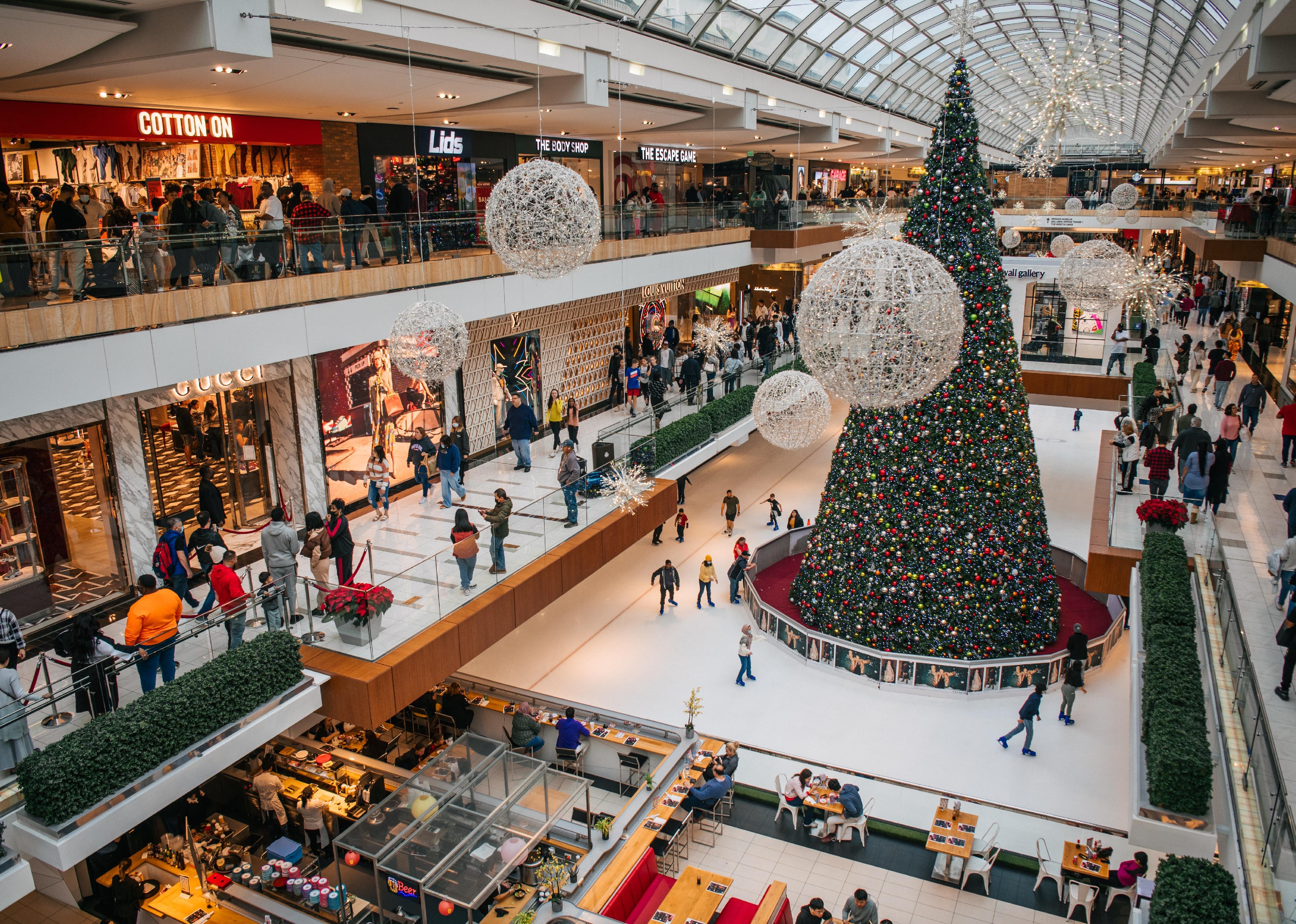 The Galleria Mall with an ice skating rink at the bottom decorated with Christmas trees and crowded with shoppers.