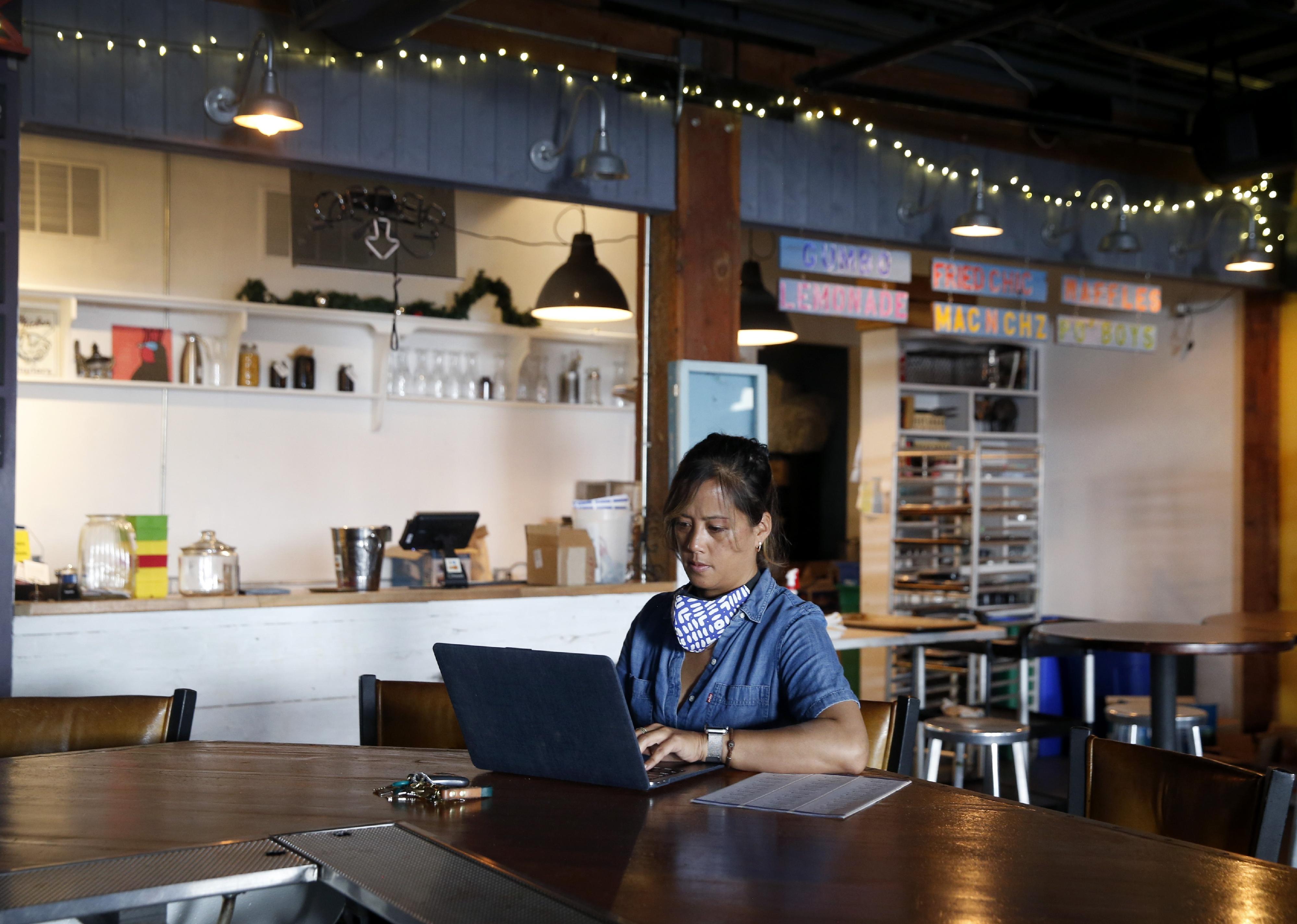 A business owner checks the status of her business loan application on her laptop at her restaurant.