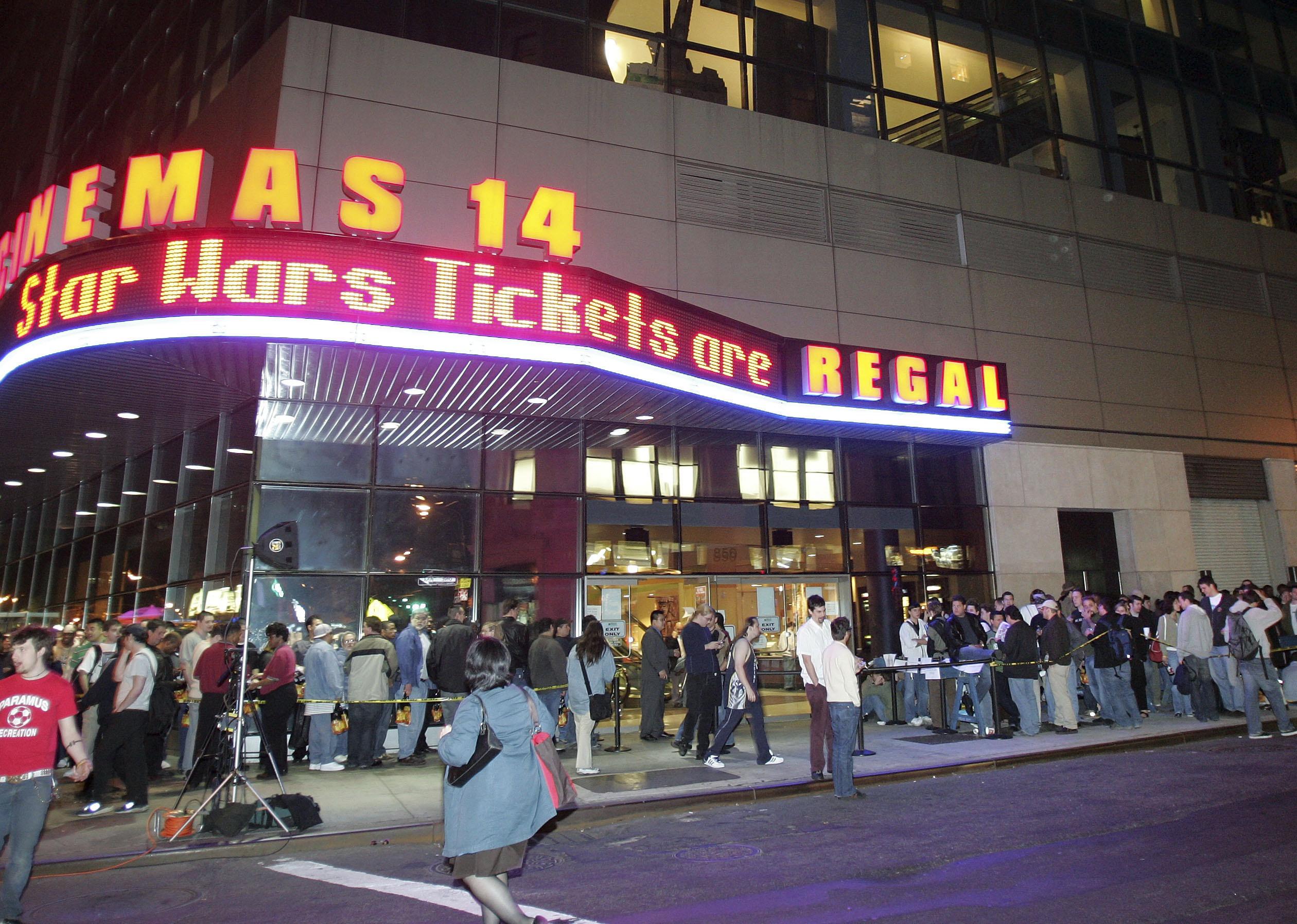 Star Wars fans line up around the outside of the theater with neon signs announcing the movie.