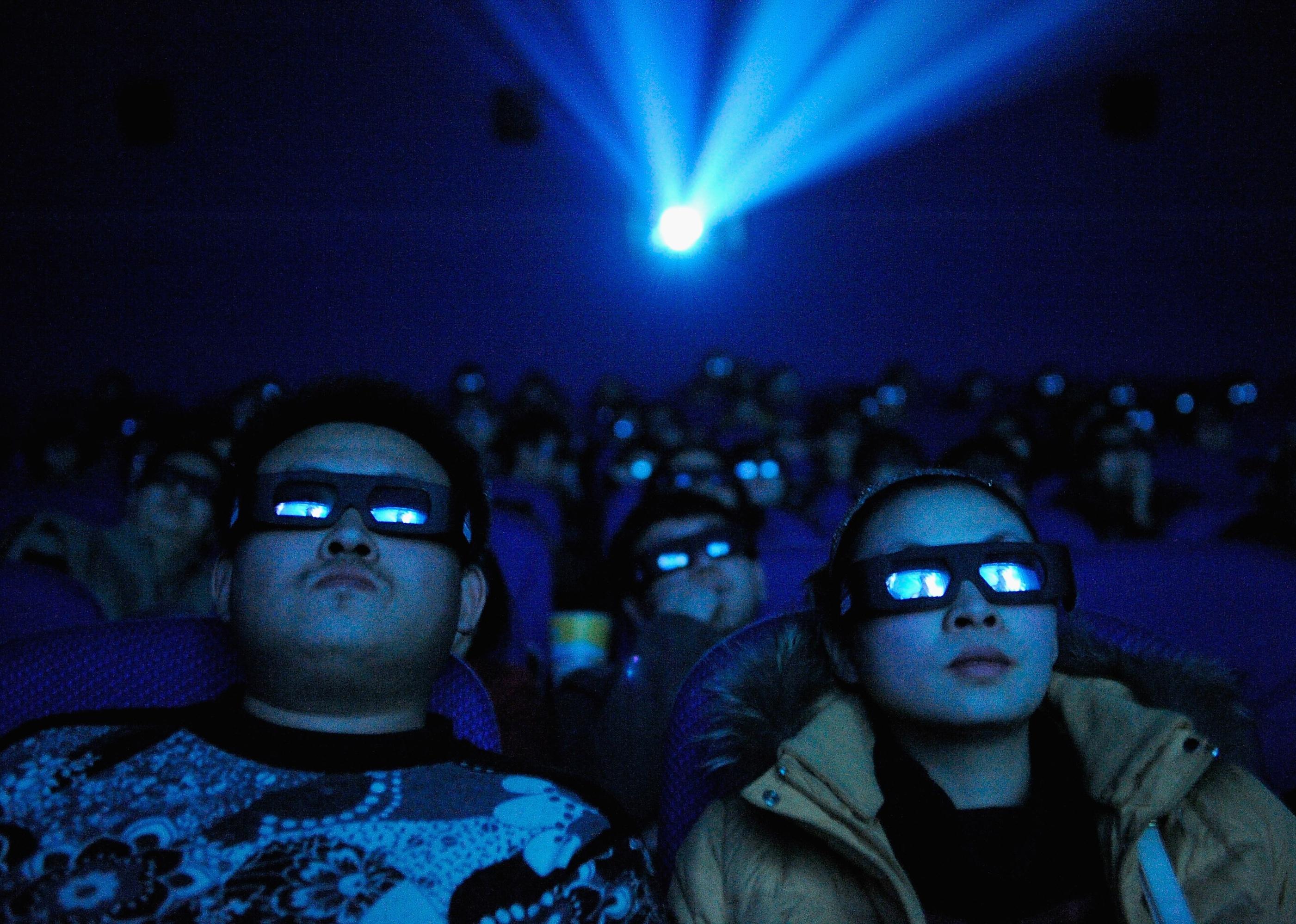 Avatar fans watching the movie with 3D glasses as blue light shines on them from the screen.