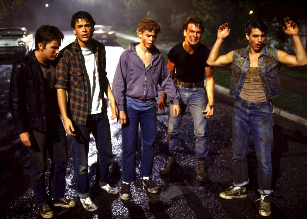 A group of young boys stand in the street in tattered and dirty clothing looking like they've been fighting.